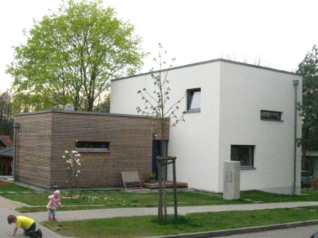 Straßenansicht: weißer Kubus und Nebengebäude mit Holzlattenfassade